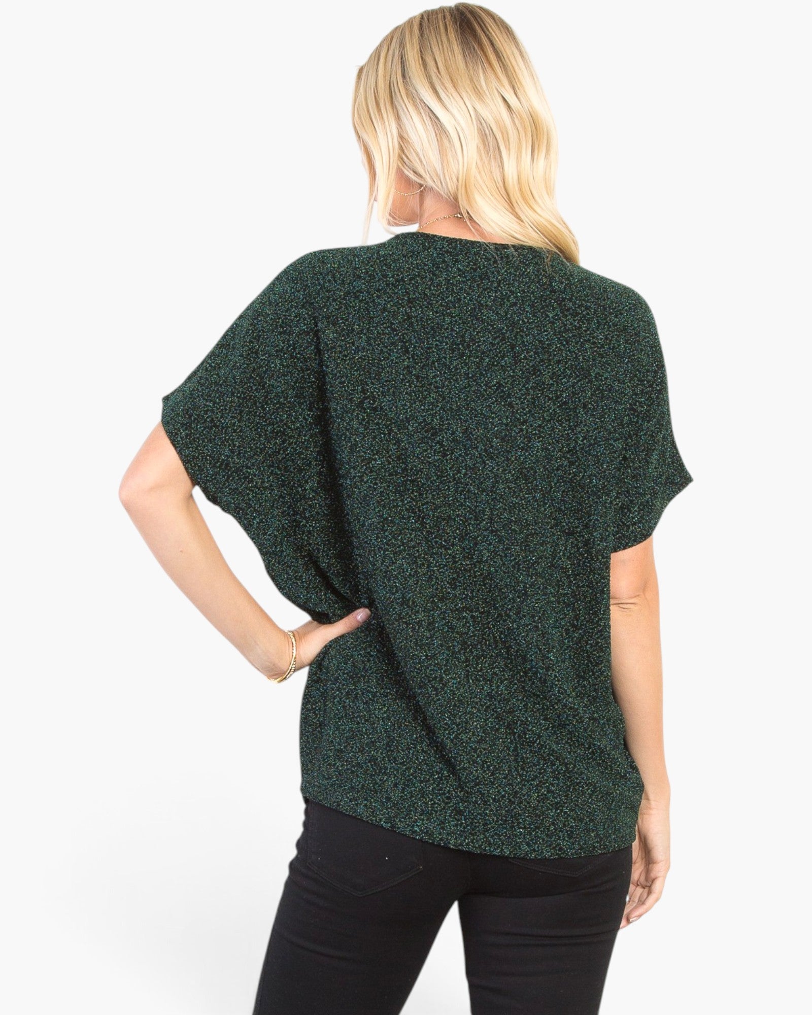 A woman shown from the back wearing a dark green short-sleeve knit top with a subtle heathered texture, paired with black pants, against a plain white studio background.