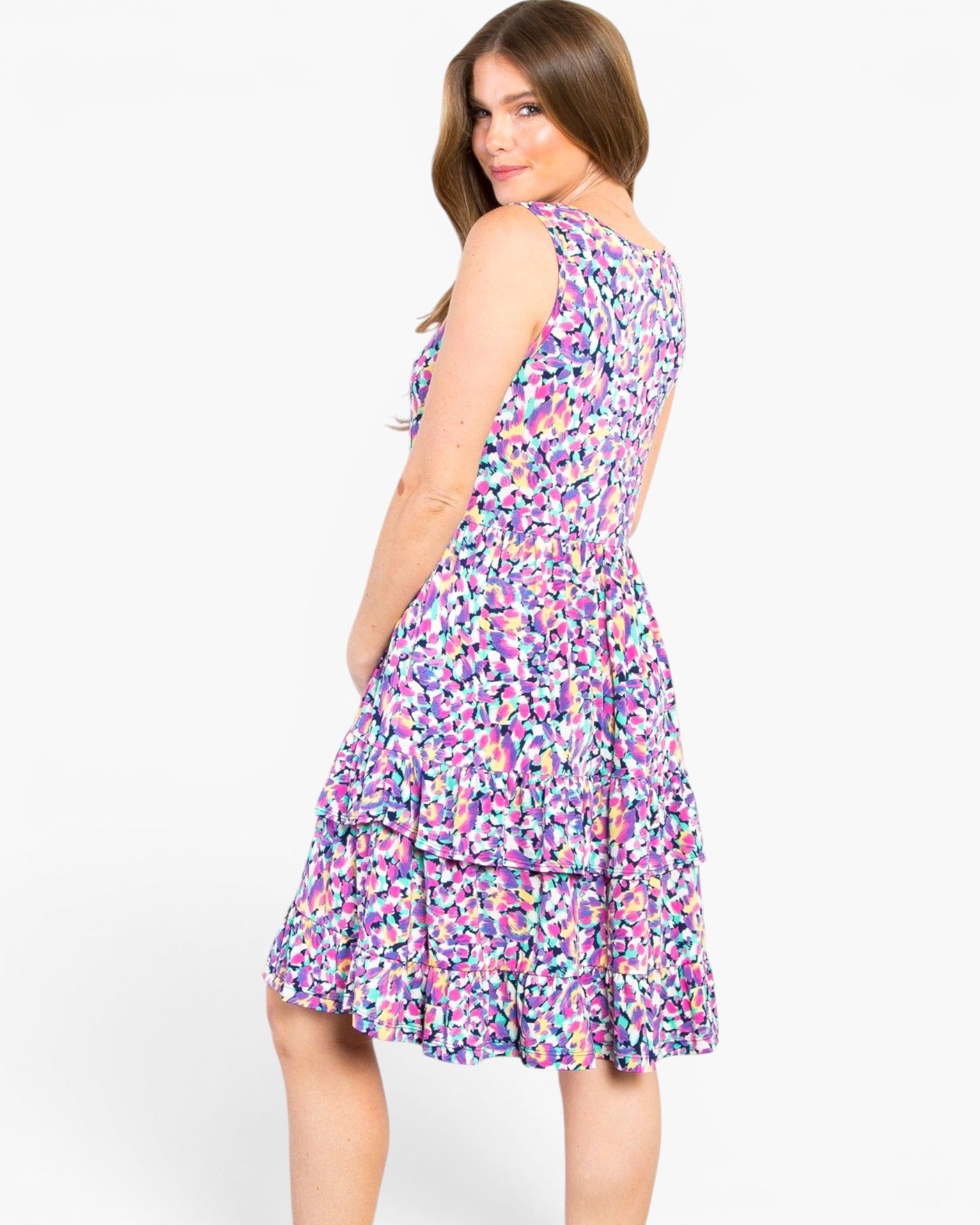 A woman modeling a sleeveless tiered A-line dress with a colorful abstract floral print in shades of purple, pink, blue, and green on a white background.