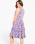 A woman modeling a sleeveless tiered A-line dress with a colorful abstract floral print in shades of purple, pink, blue, and green on a white background.
