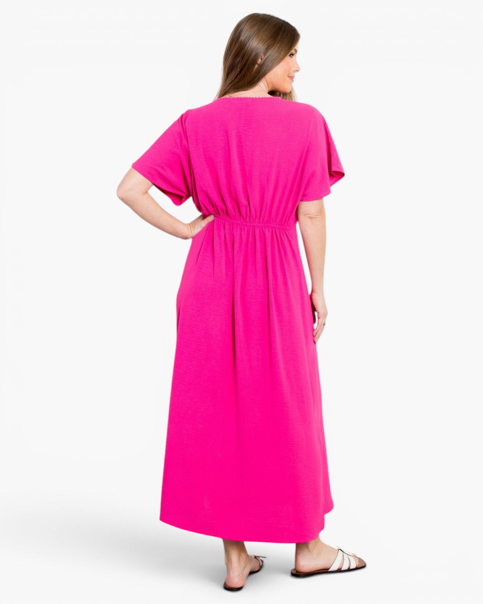 A woman wearing a bright pink short-sleeve maxi dress, shown from the back against a plain white studio background.