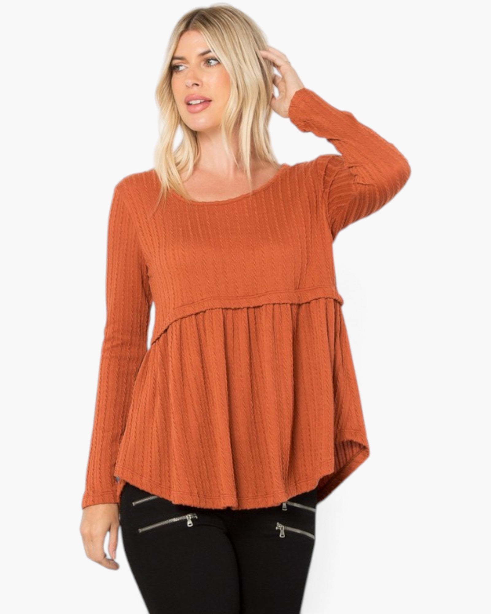A woman modeling a rust-orange ribbed knit long-sleeve top with a peplum waist, paired with black pants, against a plain white background.