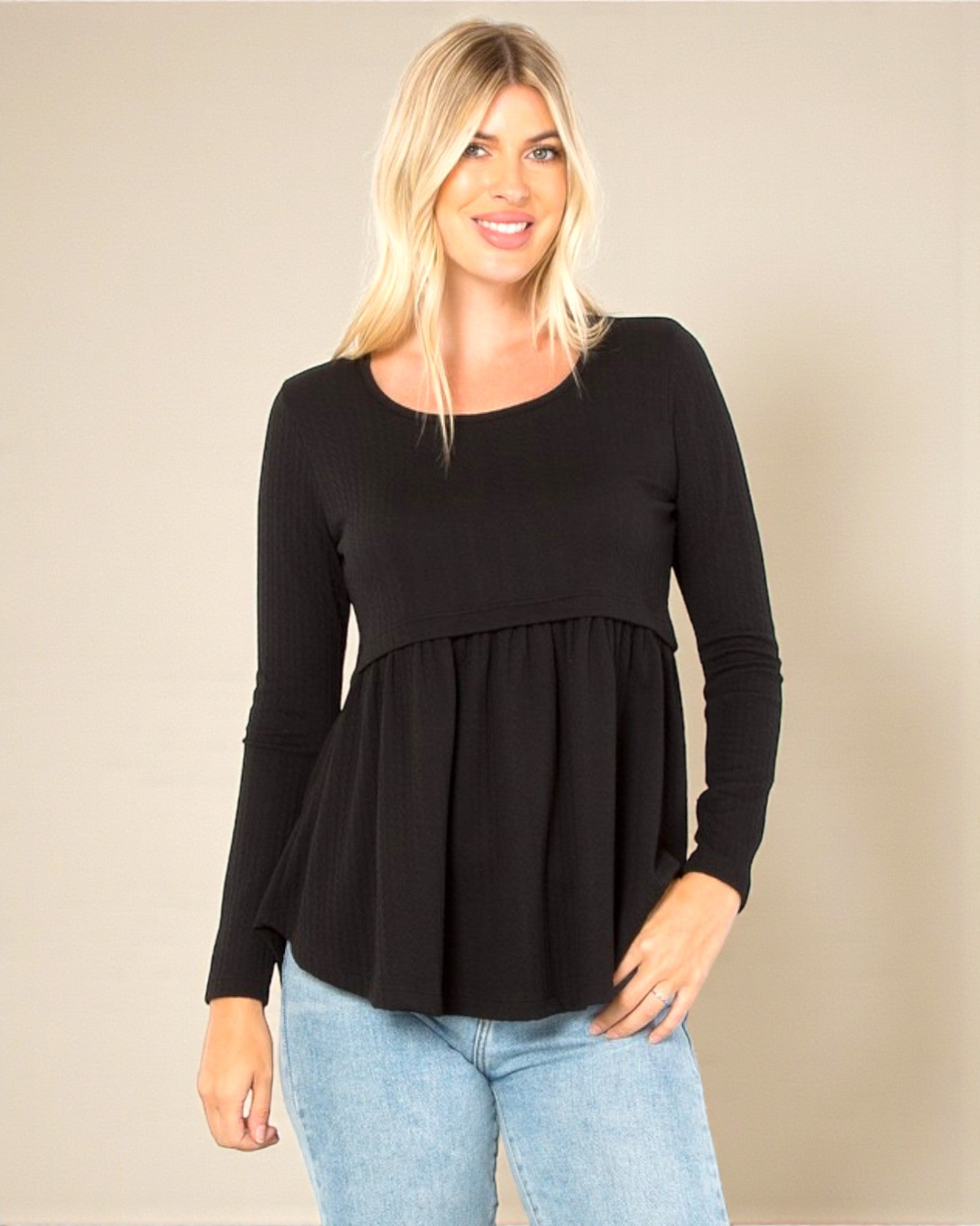 Woman wearing a black long-sleeve top and light blue jeans against a beige background