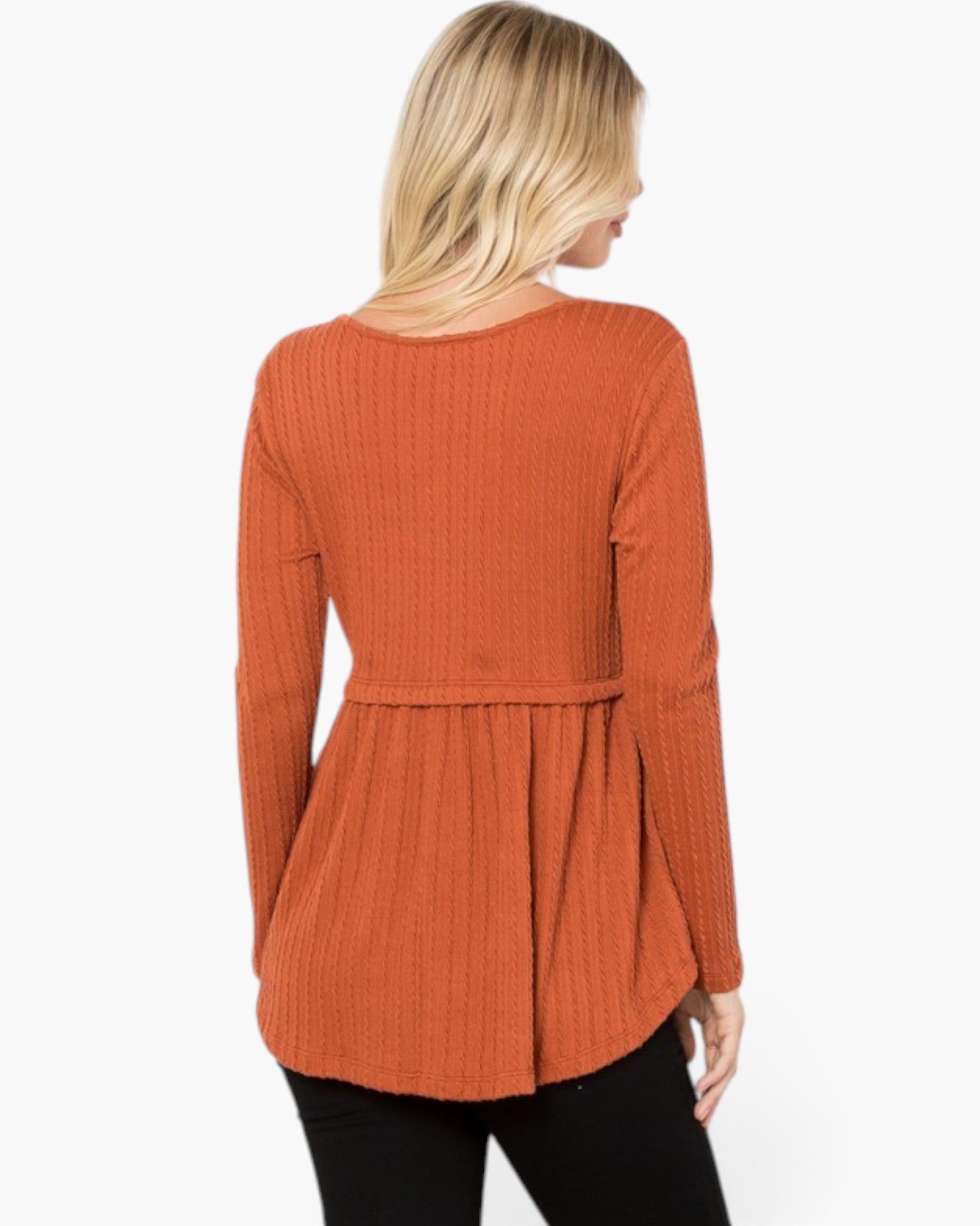 A woman shown from the back wearing a ribbed knit long-sleeve top in a burnt orange color, paired with black pants, against a plain white background.