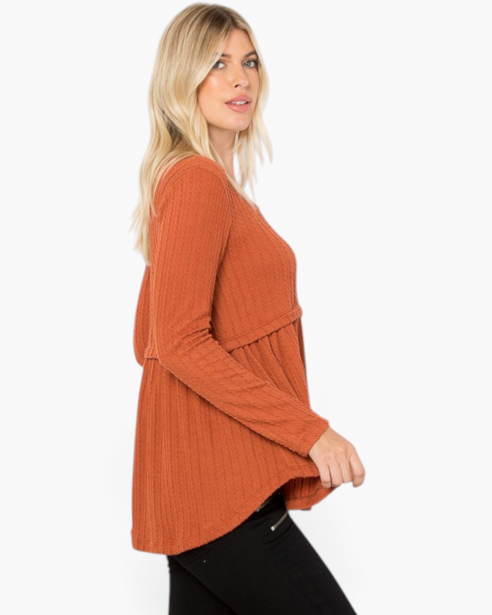 A woman wearing a rust-orange ribbed knit long-sleeve top, shown from a side profile against a plain white background.