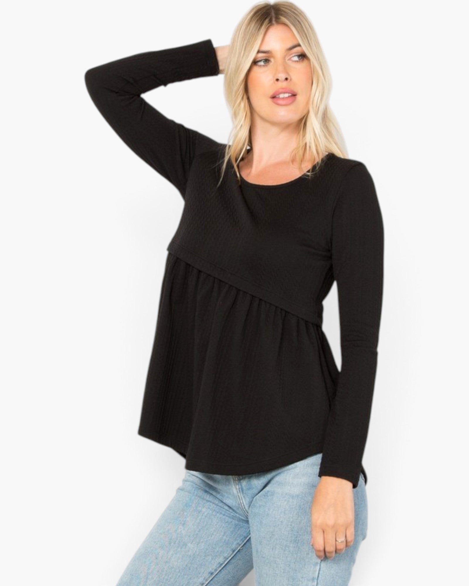 A woman modeling a black long-sleeve top with a peplum waist, paired with light blue jeans, against a plain white background.
