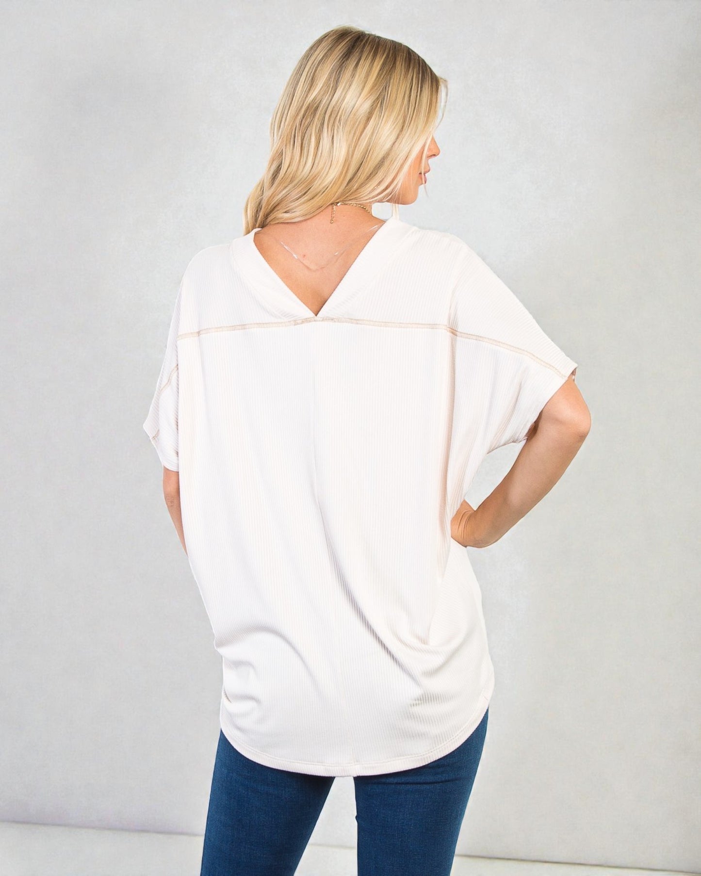 Woman wearing a white blouse with a V-neck and short sleeves, standing against a plain background.