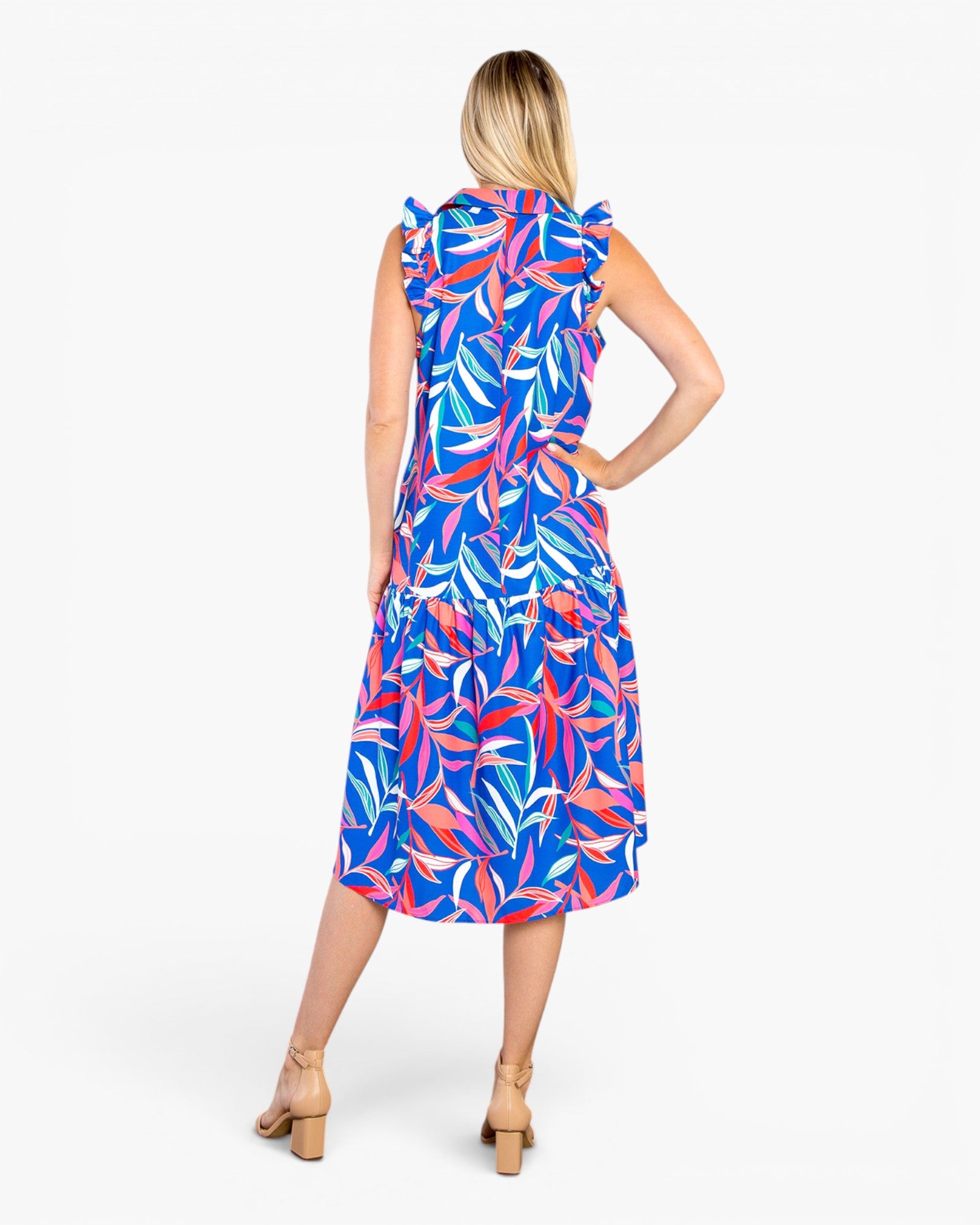 A woman modeling a sleeveless midi dress with a vibrant tropical leaf print in blue, pink, and white, shown from the back against a plain white background.