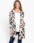 A woman modeling a long-sleeve open-front cardigan with an abstract leopard-like pattern in beige, black, and muted purple, worn over a white top and dark blue jeans against a plain white studio background.
