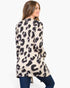 A woman shown from the back wearing a cream-colored long-sleeve tunic top with a black and dark purple leopard print, paired with dark blue jeans, against a plain white background.