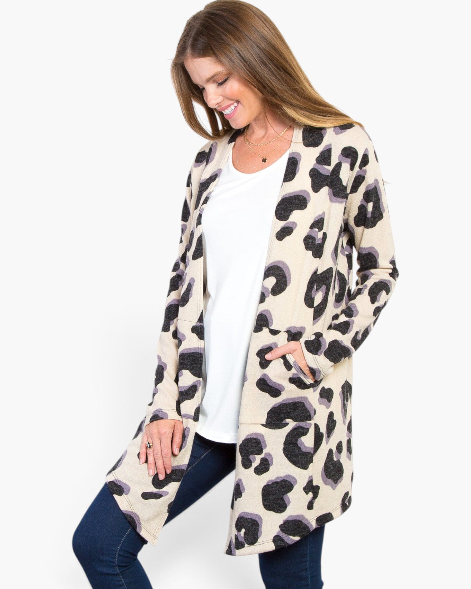 A woman modeling a long-sleeve open-front cardigan with an abstract leopard-like print in beige, black, and gray, worn over a white top and dark blue jeans against a plain white background.