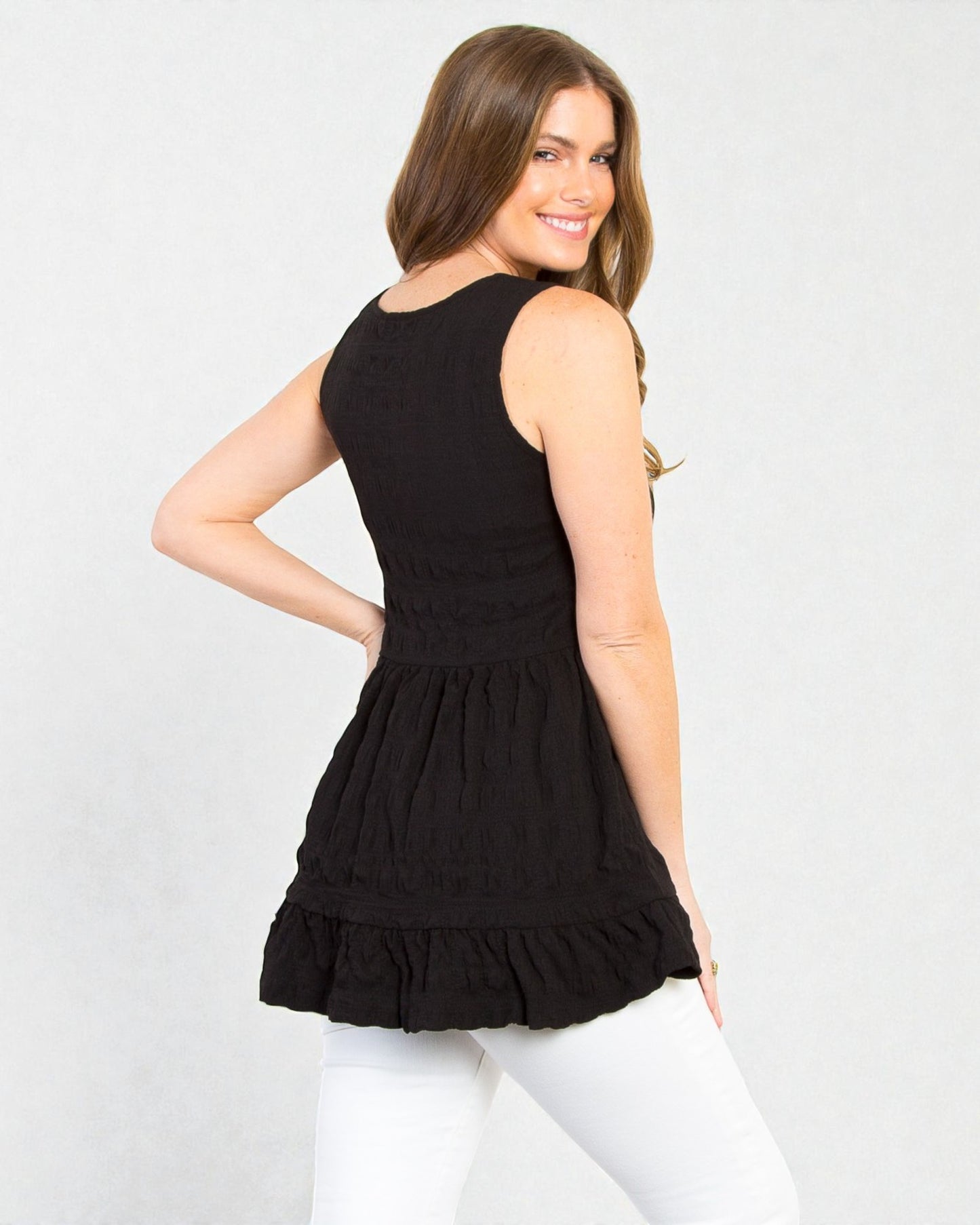 Woman wearing a black sleeveless dress with a ruffled bottom on a white background