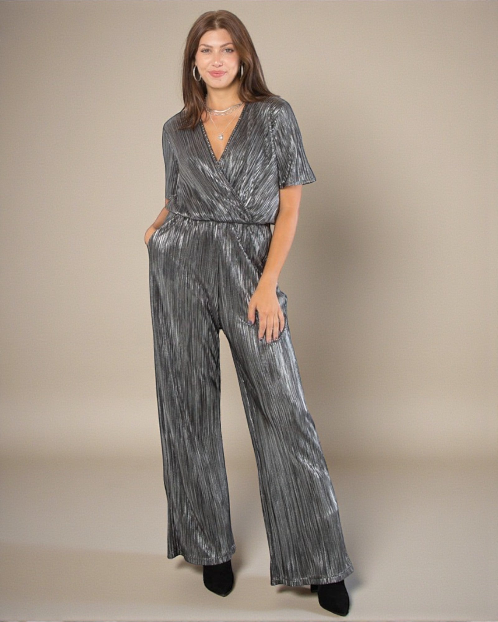 Woman wearing a silver metallic jumpsuit against a beige background