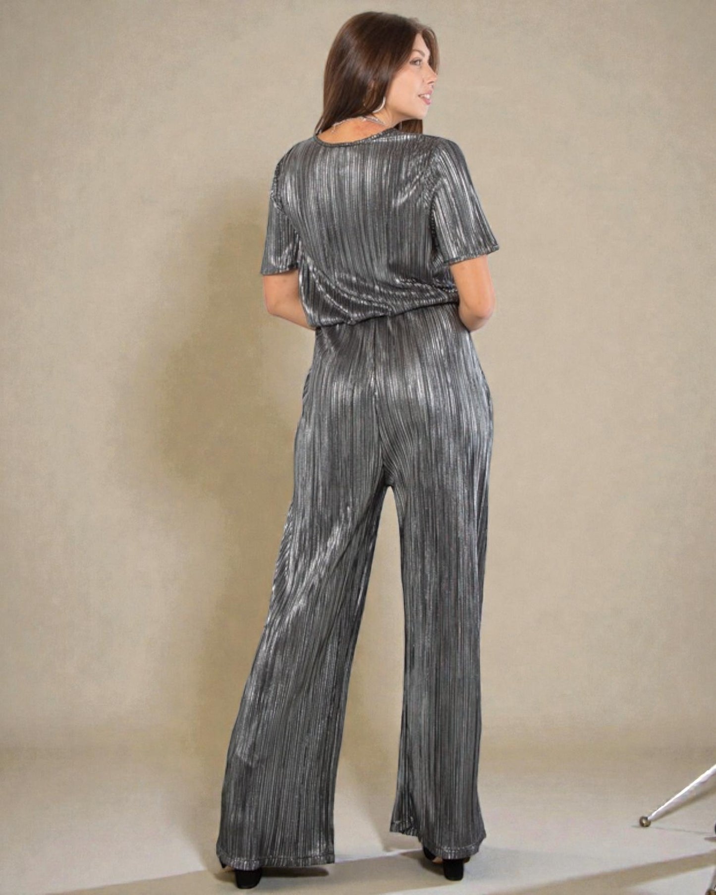 Woman wearing a silver sequin jumpsuit against a beige background