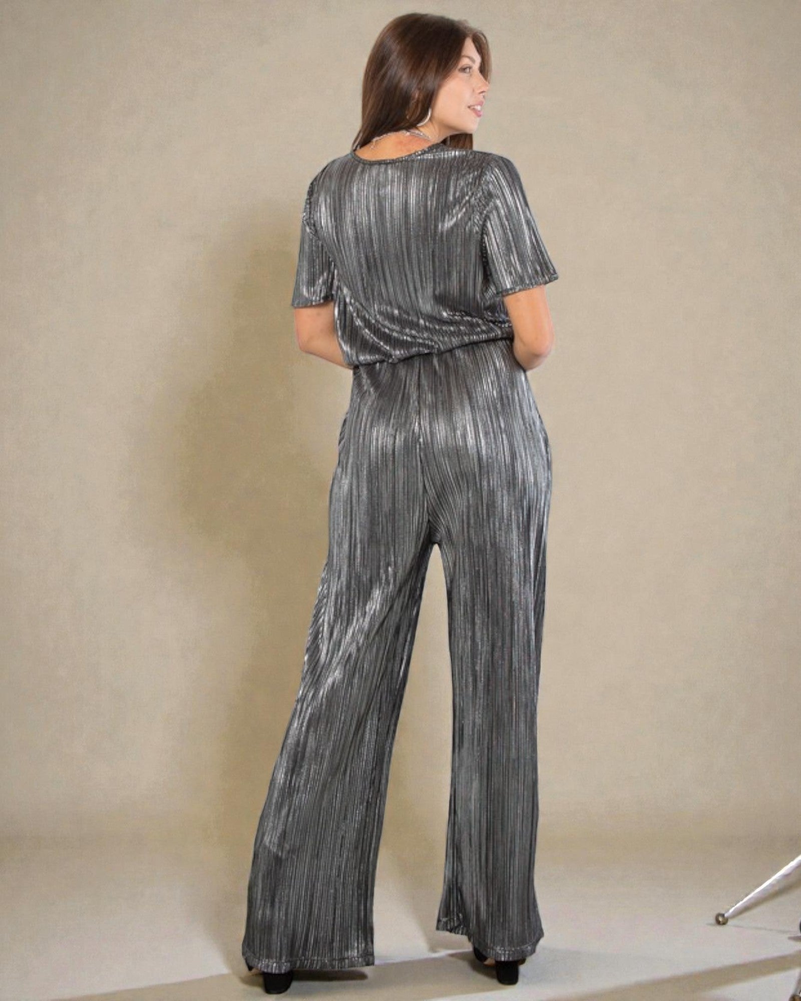 Woman wearing a silver sequin jumpsuit against a beige background