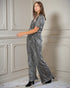 Woman wearing a gray patterned jumpsuit in a room with decorative wall paneling.
