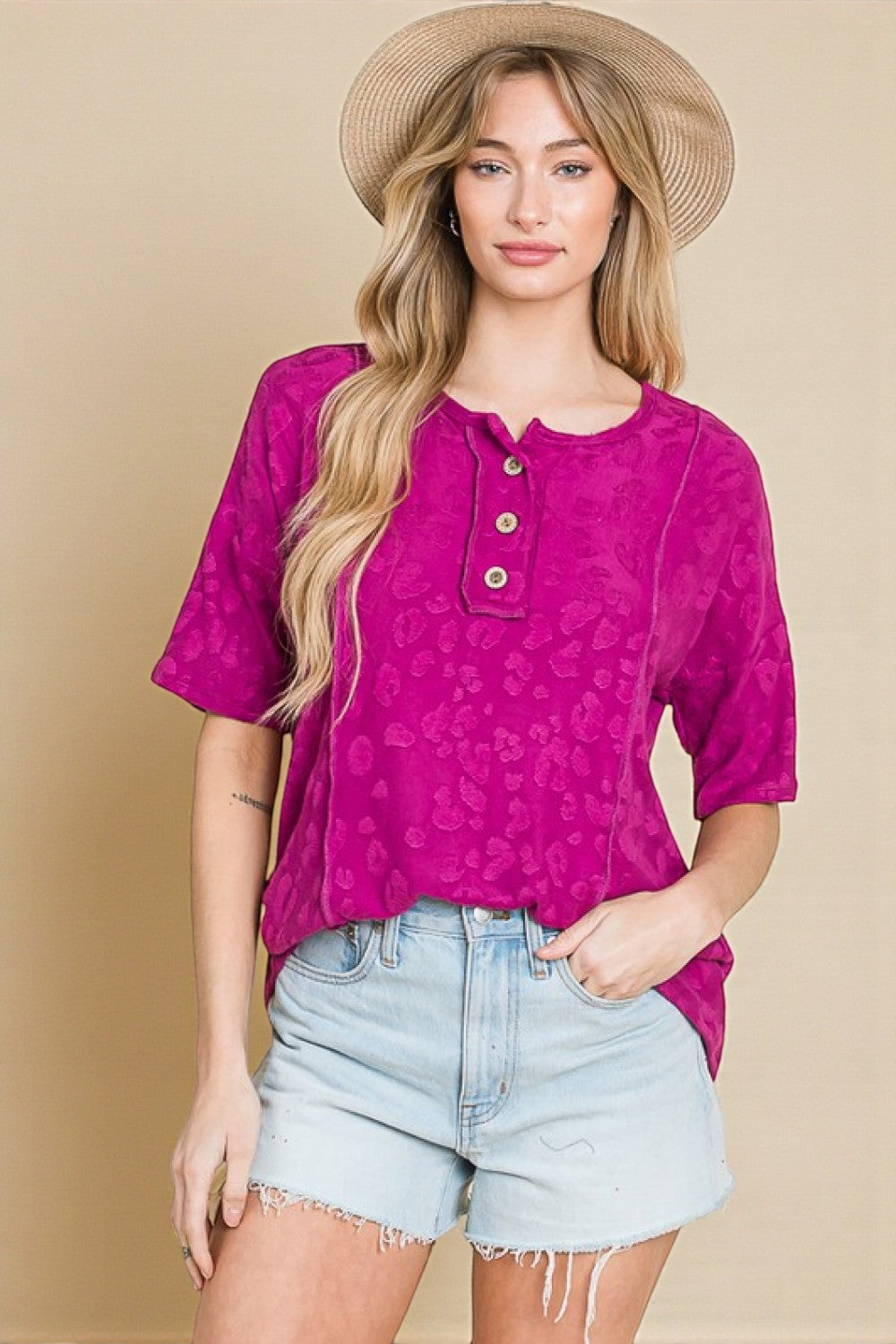 Woman wearing a pink patterned top and light blue shorts with a beige background