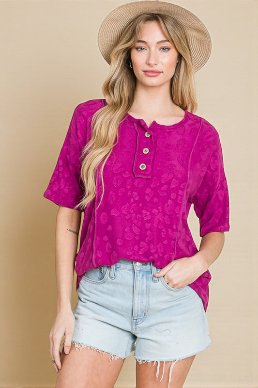 Woman wearing a pink patterned top and light blue shorts with a beige background