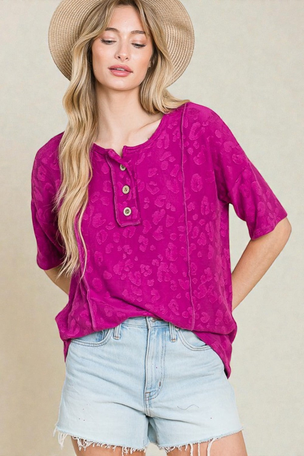 Woman wearing a pink patterned top and denim shorts against a beige background