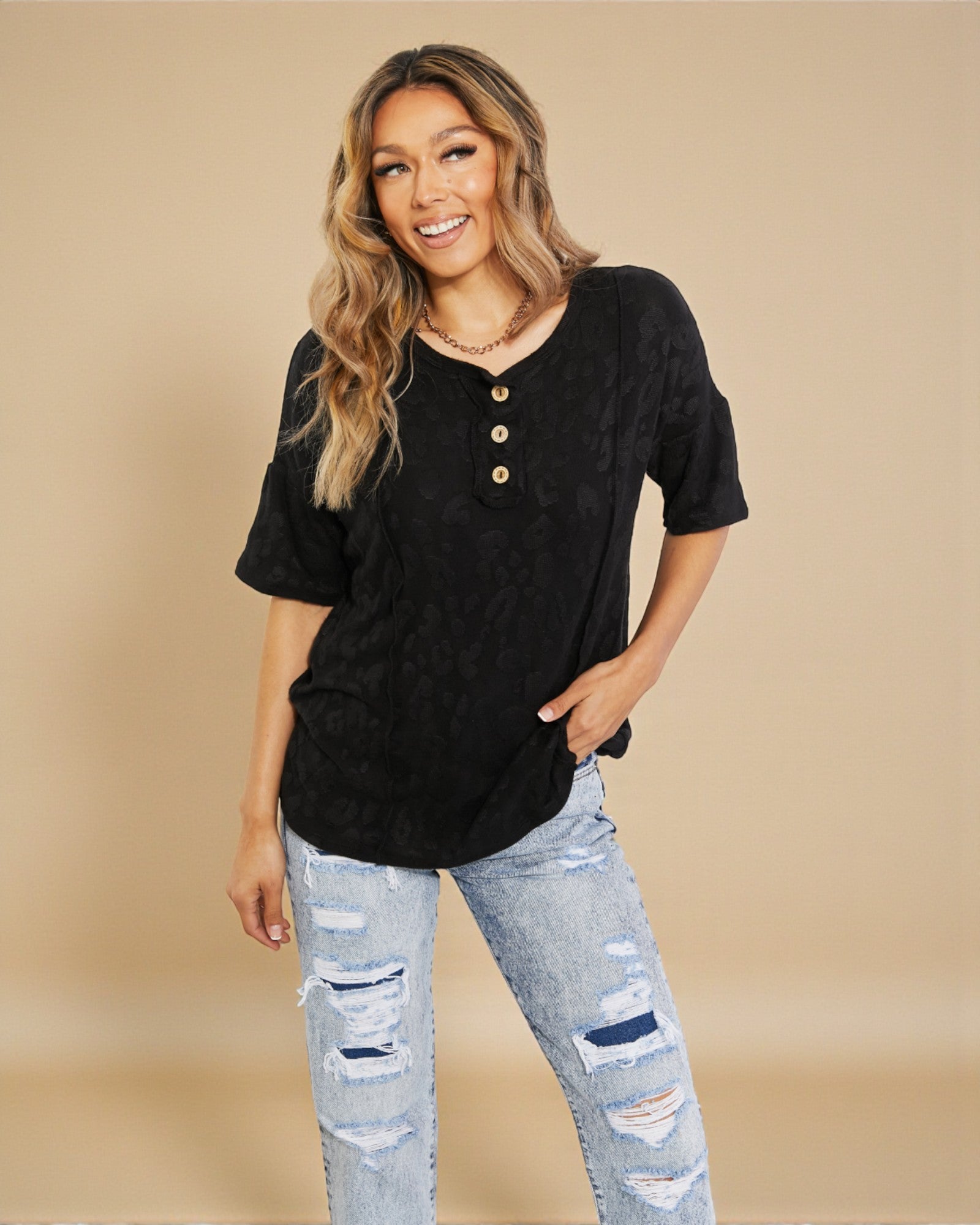 Woman wearing a black button-up shirt and ripped jeans on a beige background