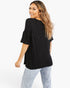 A woman wearing a black textured short-sleeve top and light-wash distressed jeans, photographed from the back against a plain white studio background.