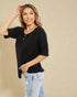 Woman wearing a black top and light blue jeans against a beige background