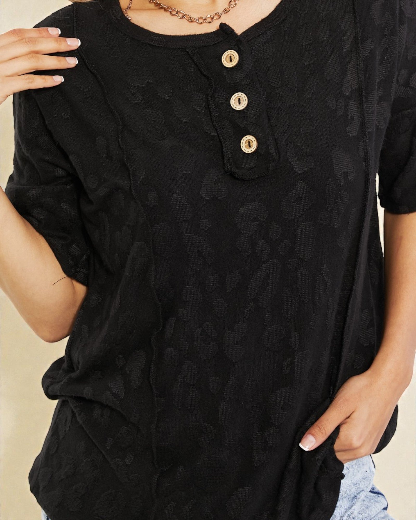 Black patterned shirt with gold buttons worn by a person on a beige background