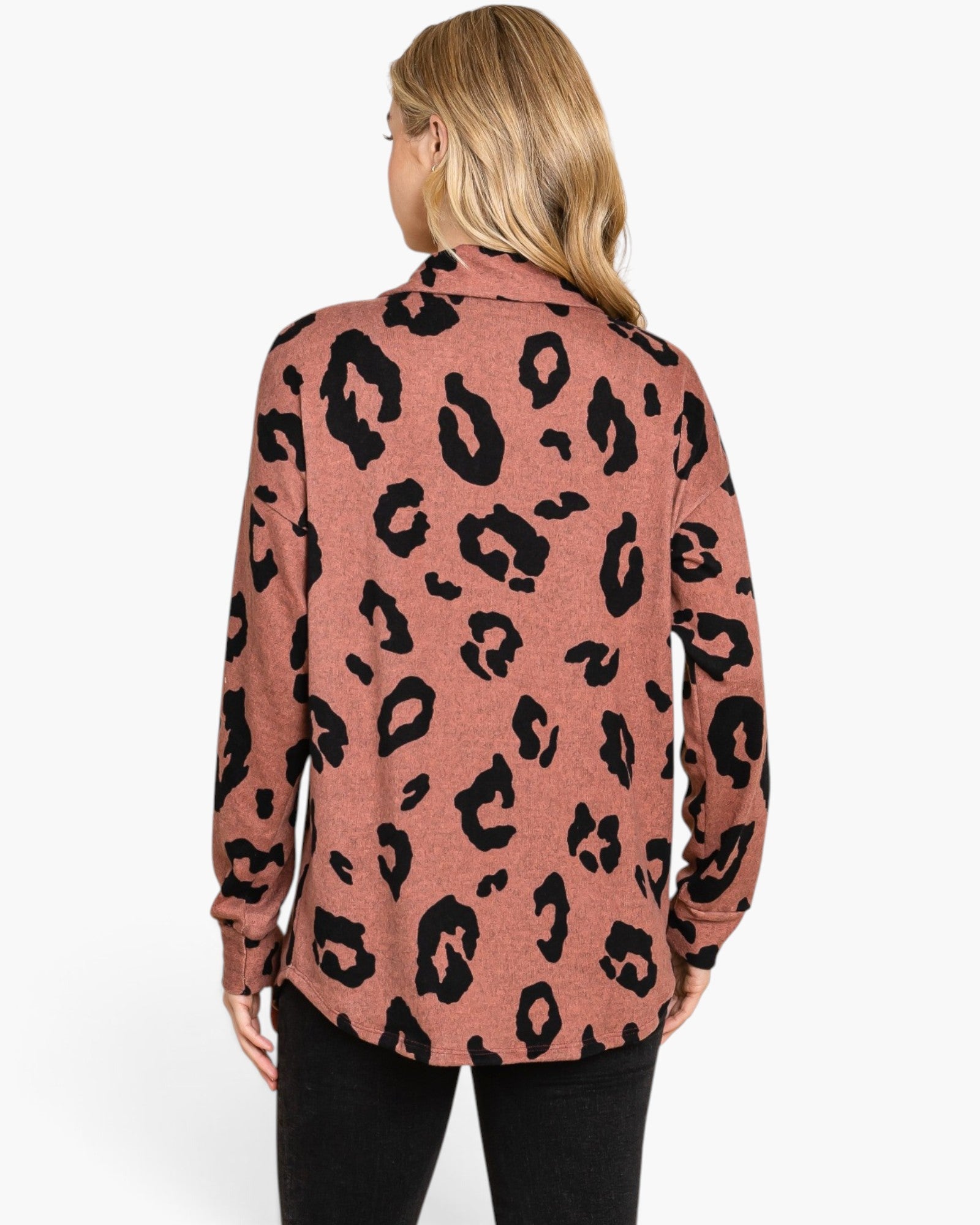 A woman viewed from the back wearing a long-sleeve collared top with a black leopard print on a dusty rose pink background, paired with black pants, against a plain white studio background.