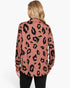 A woman viewed from the back wearing a long-sleeve collared top with a black leopard print on a dusty rose pink background, paired with black pants, against a plain white studio background.