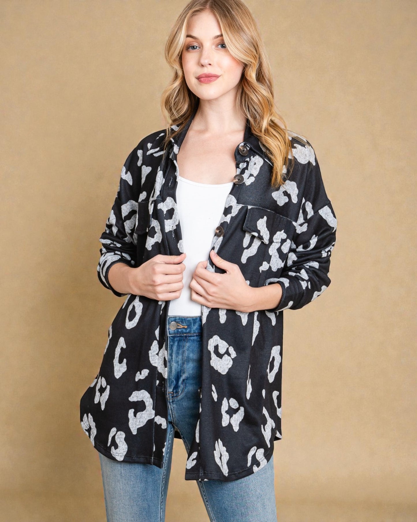 Woman wearing a black leopard print jacket over a white top and blue jeans on a beige background