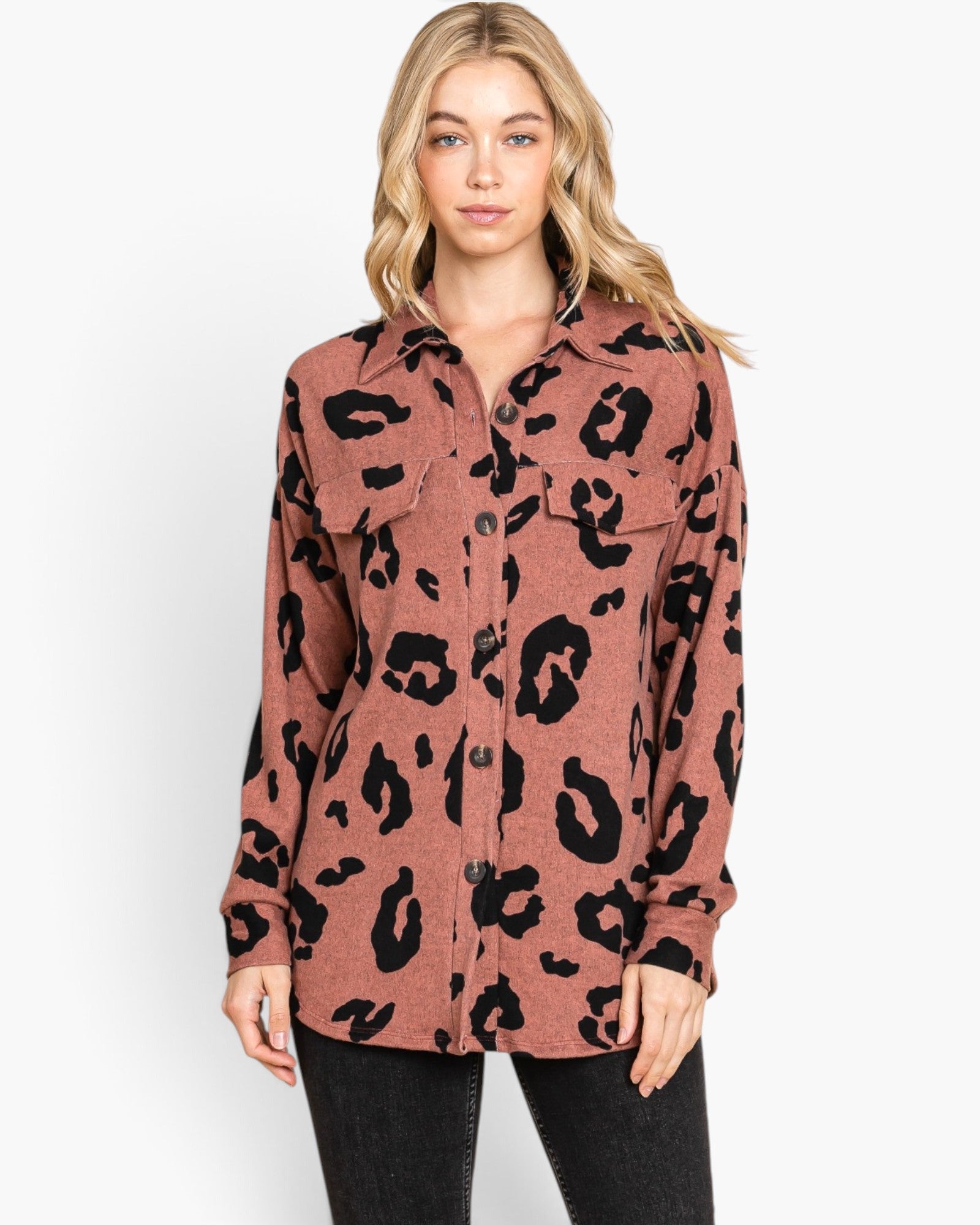 A woman modeling a long-sleeve button-up shirt with a black leopard print on a dusty rose base, paired with black jeans against a plain white studio background.