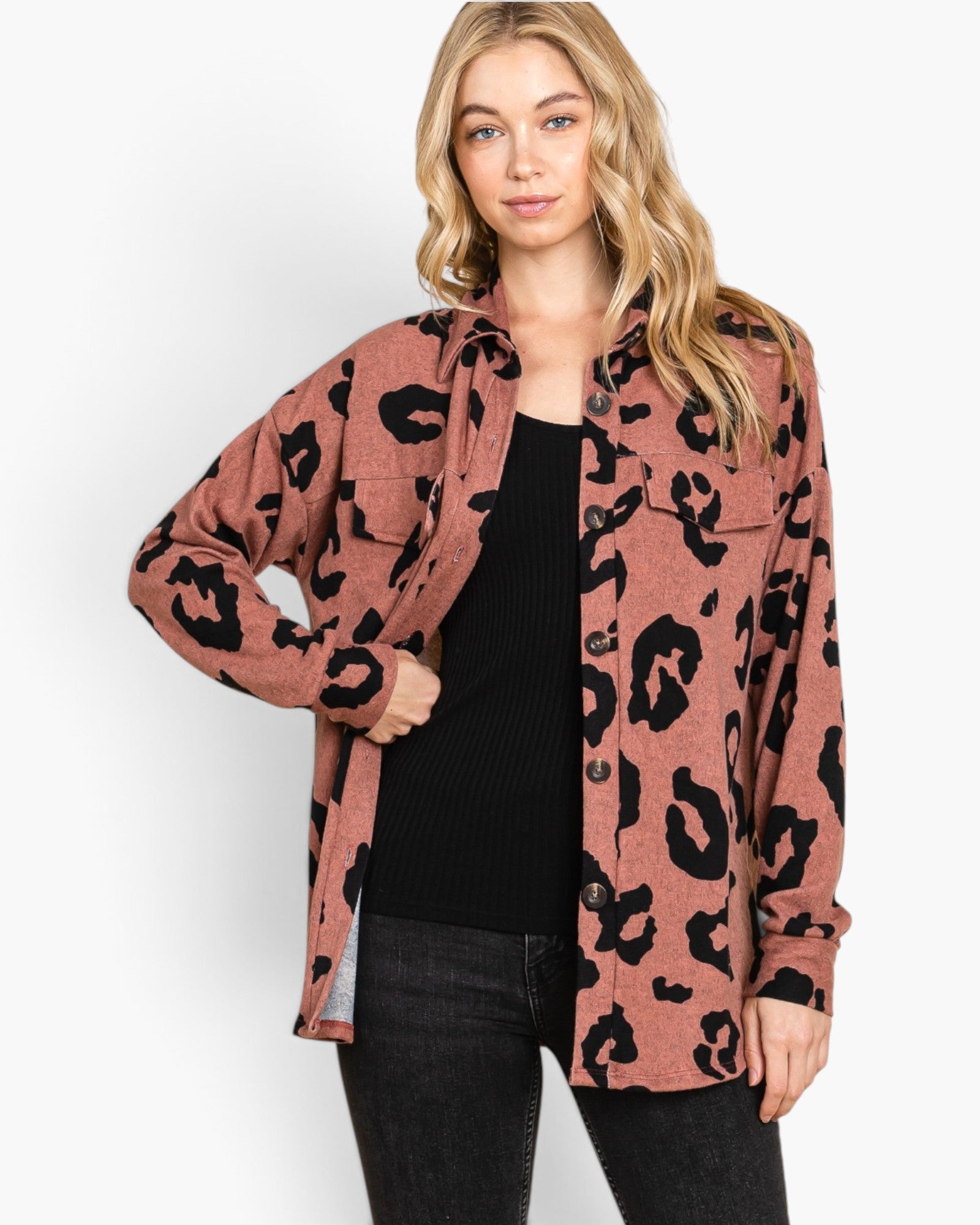 A woman modeling a dusty rose leopard-print button-up shirt over a black ribbed top and black jeans, photographed against a clean white studio background.