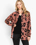 A woman modeling a dusty rose leopard-print button-up shirt over a black ribbed top and black jeans, photographed against a clean white studio background.