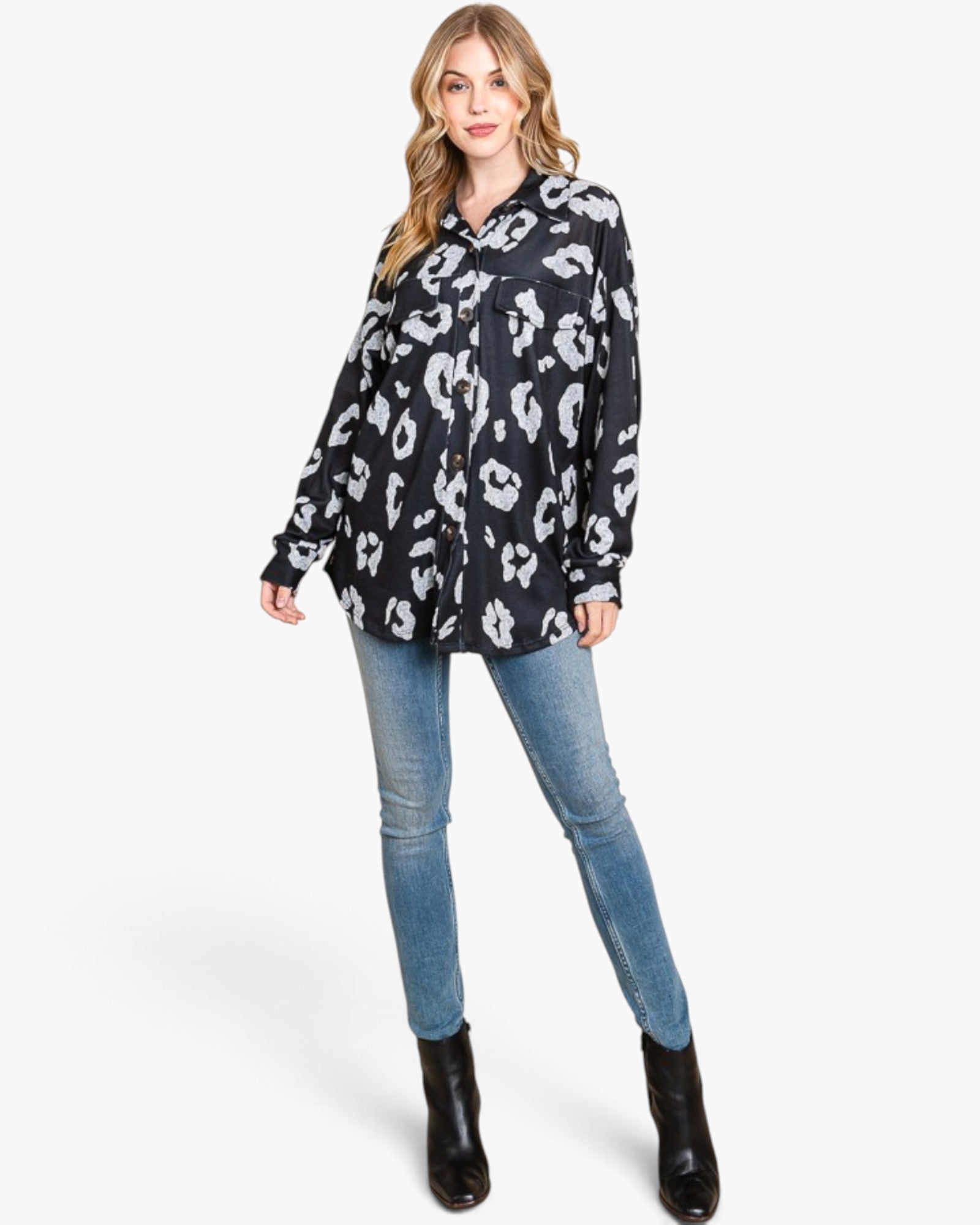 A woman modeling a black button-up shirt with a white abstract animal-like print, paired with blue skinny jeans and black ankle boots, against a light gray studio background.