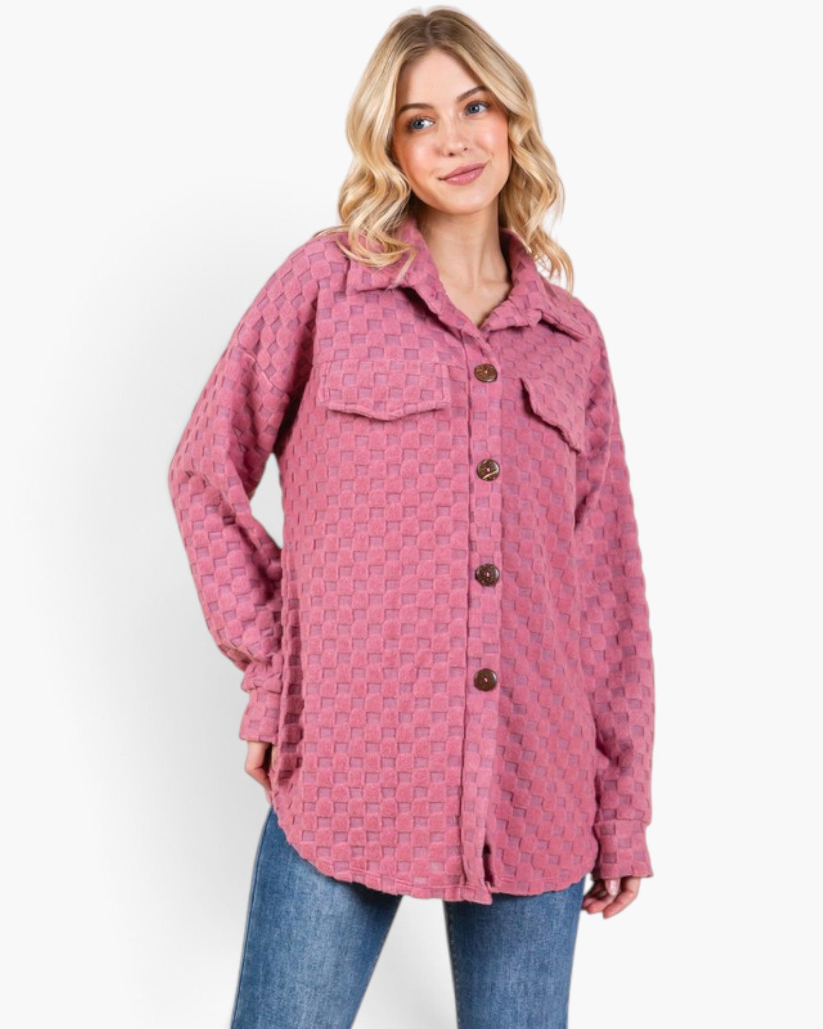 A woman modeling a pink textured, long-sleeve button-up shirt jacket with a subtle geometric pattern, paired with blue jeans, against a plain white background.