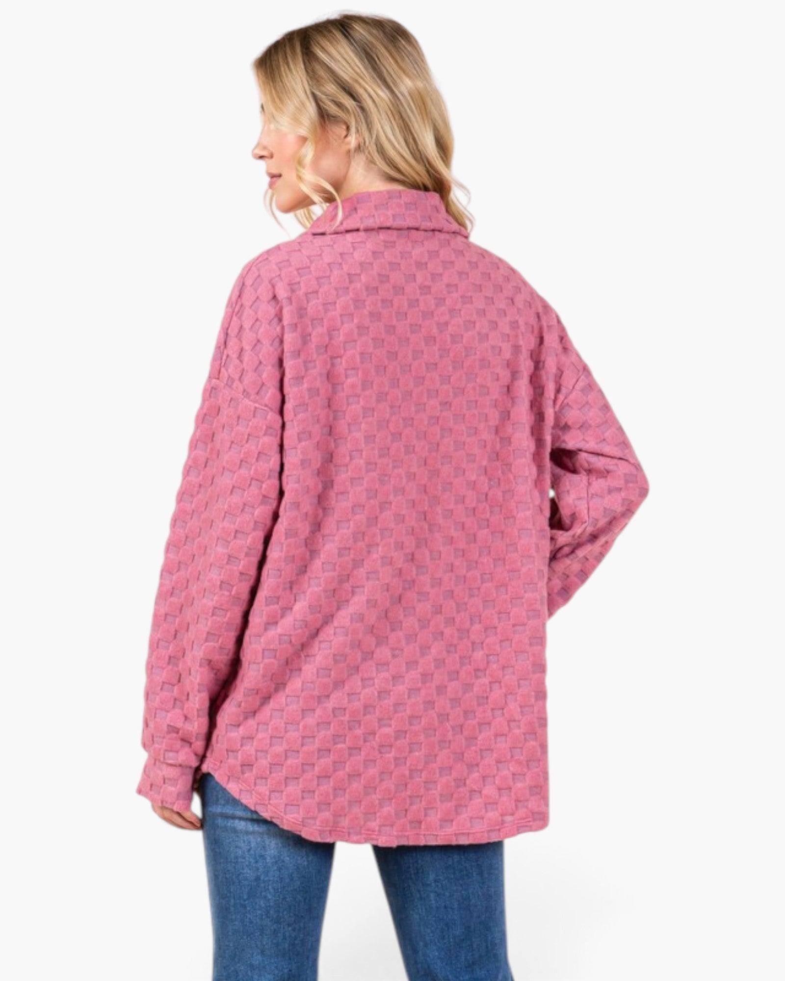 A woman shown from the back wearing a pink long-sleeve button-up shirt with a subtle geometric pattern, paired with blue jeans, against a plain white background.