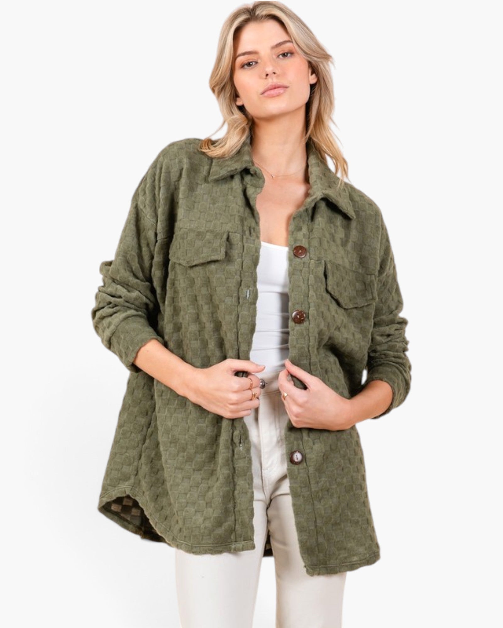 A woman wearing an oversized olive green quilted button-up shirt jacket over a white top and white pants, photographed against a clean white studio background.
