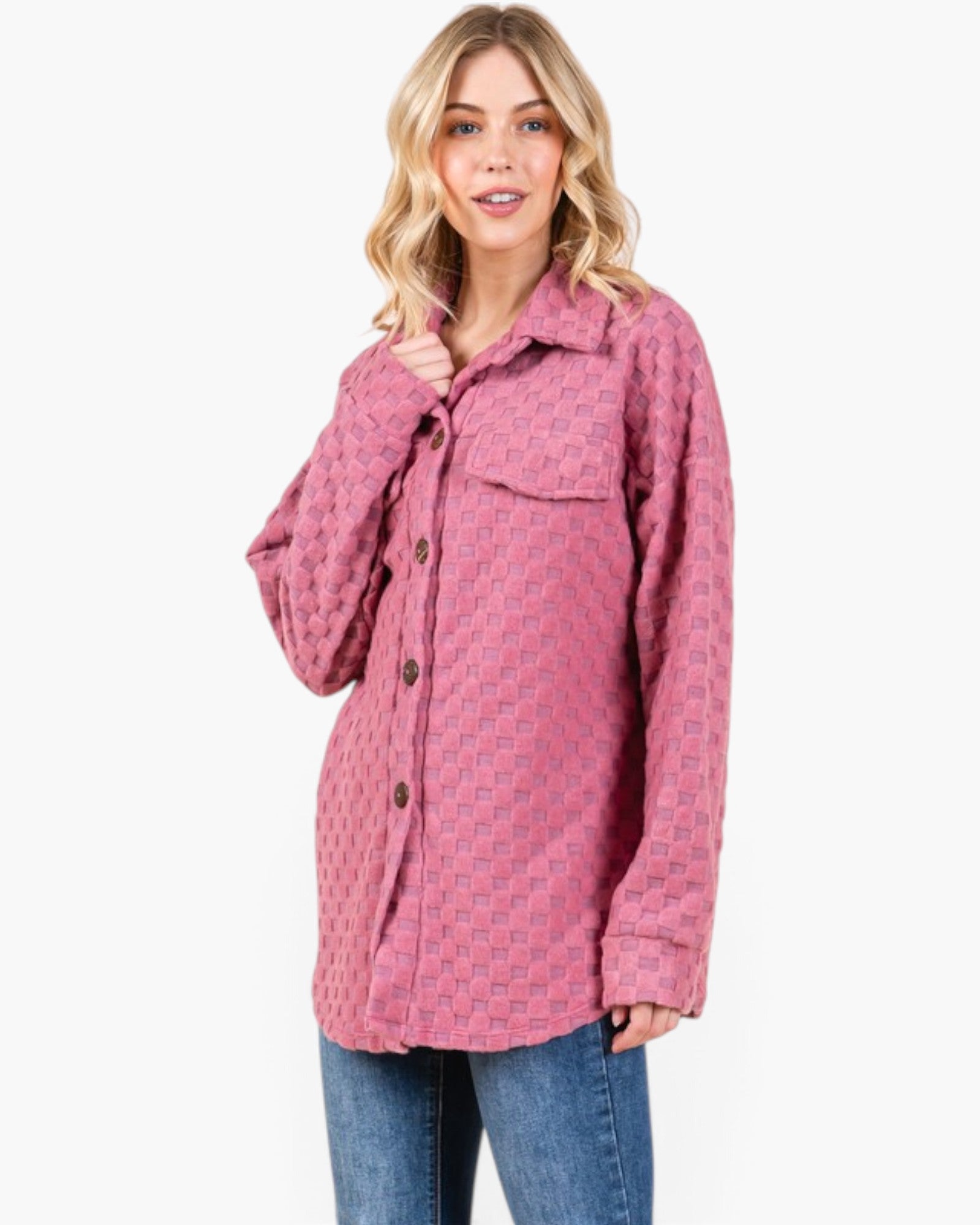 A woman modeling a pink patterned button-up shirt jacket with blue jeans against a plain white background.