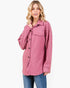A woman modeling a pink patterned button-up shirt jacket with blue jeans against a plain white background.