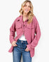 A woman modeling a pink quilted button-up shirt jacket with a subtle geometric pattern, worn over a white t-shirt and blue jeans, against a plain white background.