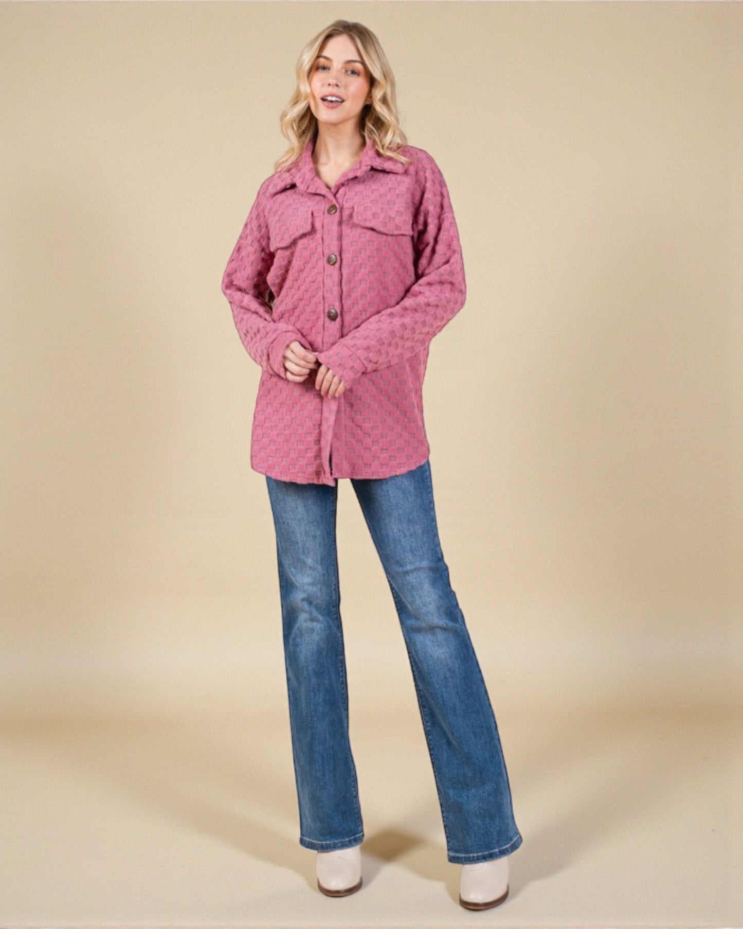 Woman wearing a pink quilted jacket and blue jeans on a beige background