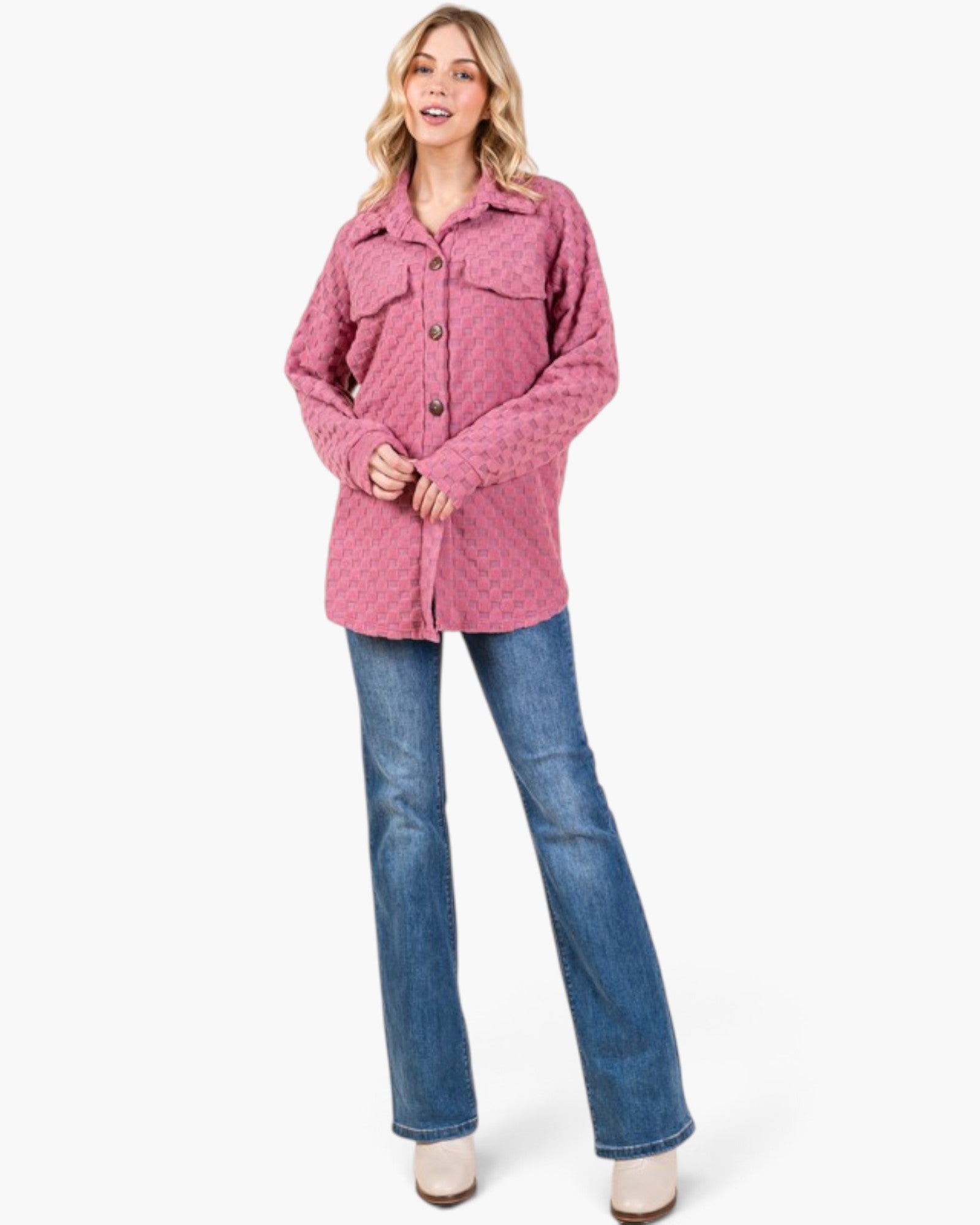 A woman modeling a pink quilted button-up shirt jacket with blue jeans and white boots against a plain white background.