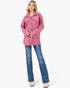 A woman modeling a pink quilted button-up shirt jacket with blue jeans and white boots against a plain white background.