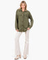 A woman modeling an olive green quilted button-up shirt with brown buttons, paired with cream flared pants and beige heeled boots, against a plain white studio background.