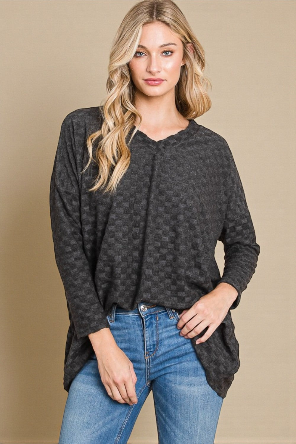 Woman wearing a dark patterned long-sleeve top and blue jeans against a beige background