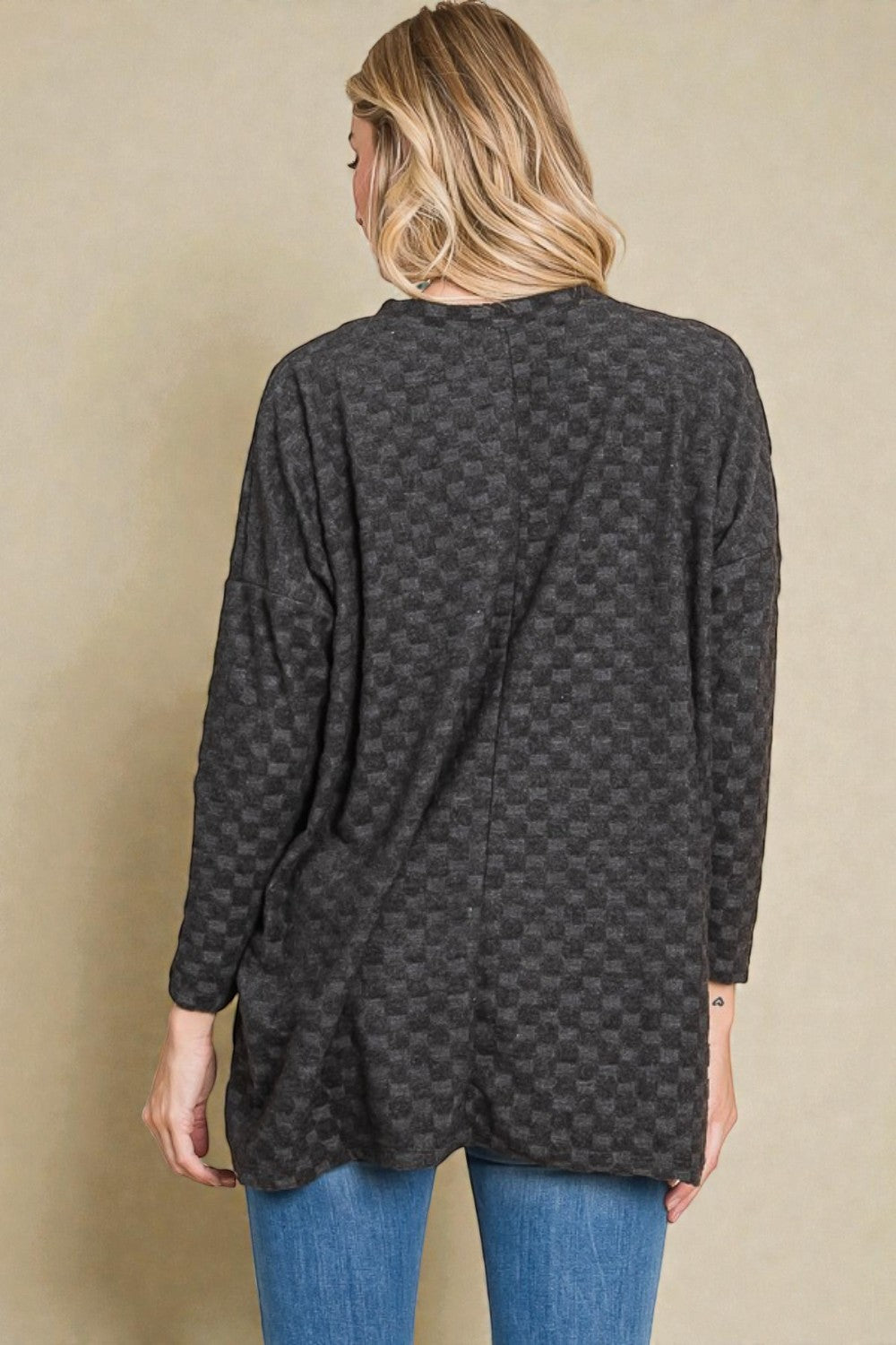 Person wearing a dark patterned long-sleeve top against a beige background