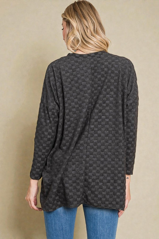 Person wearing a dark patterned long-sleeve top against a beige background