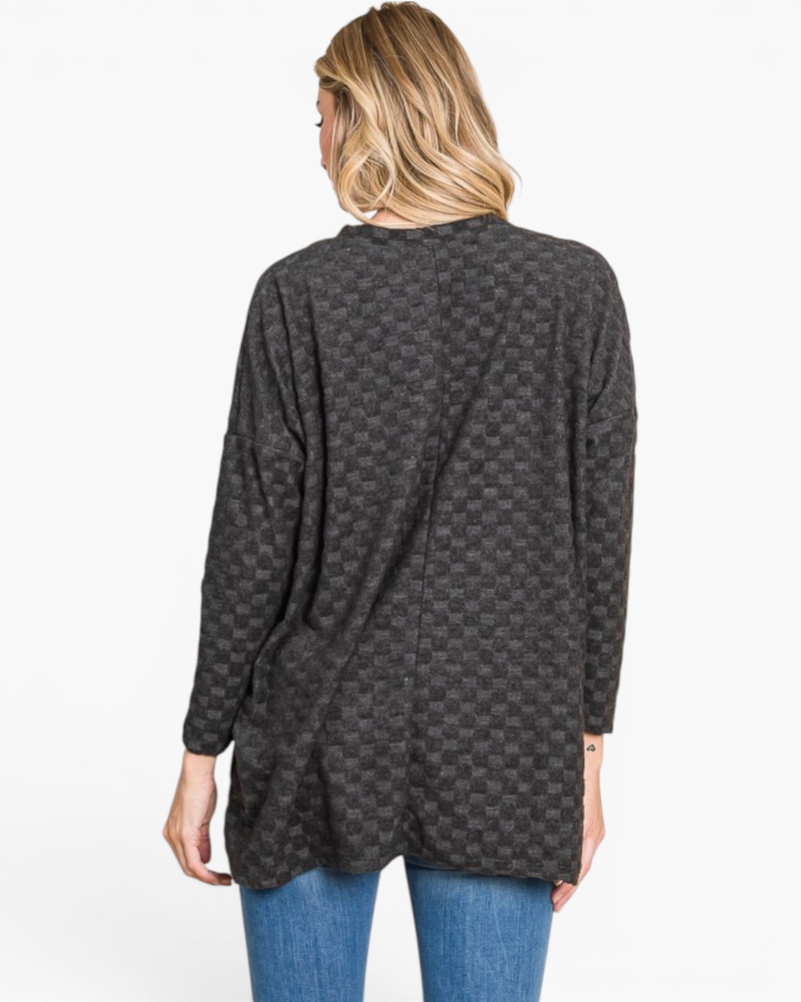 A woman viewed from the back wearing a dark charcoal gray long-sleeve tunic top with a subtle checkerboard pattern, paired with blue jeans, against a plain white background.