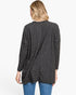 A woman viewed from the back wearing a dark charcoal gray long-sleeve tunic top with a subtle checkerboard pattern, paired with blue jeans, against a plain white background.