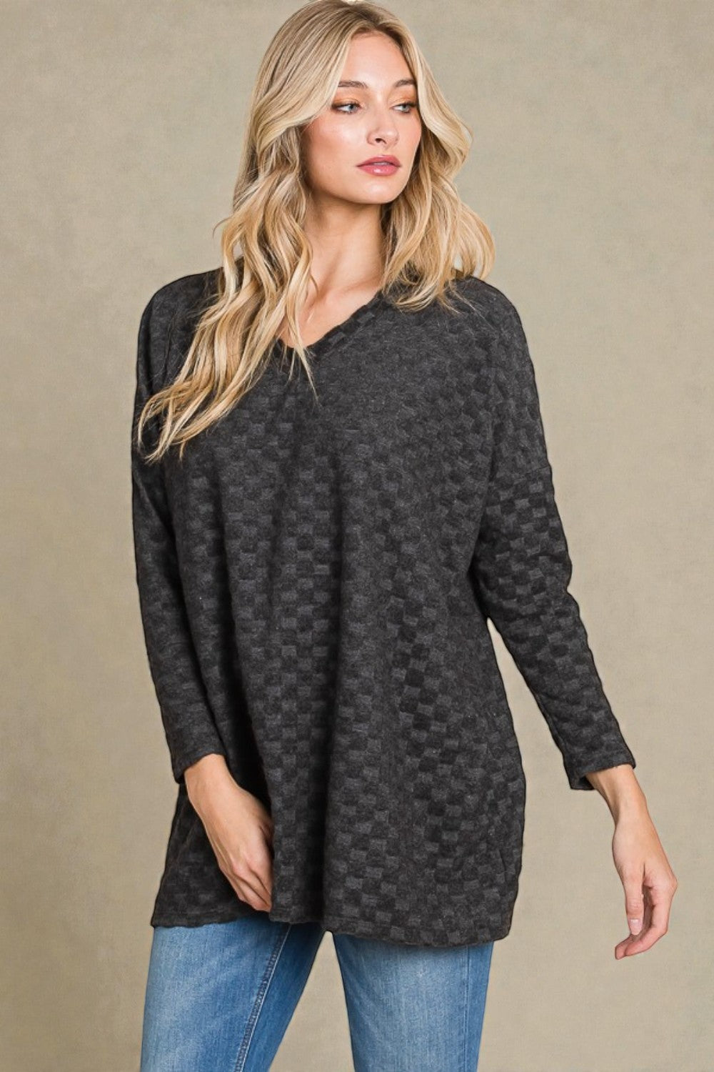 Woman wearing a dark gray patterned sweater and blue jeans on a beige background