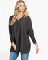 A woman modeling a dark gray long-sleeve knit tunic top with a subtle checkerboard pattern, paired with blue jeans, against a plain white studio background.